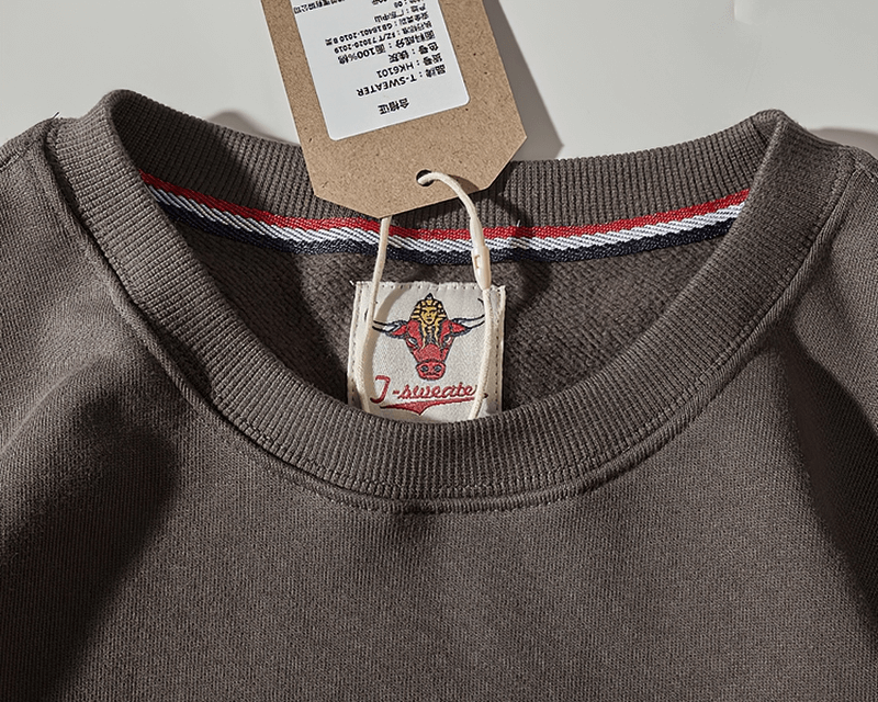 Close-up of a solid color round neck sweatshirt with a kangaroo pocket and tag, showing detailed fabric texture.